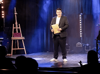 Florian Dolar allein auf einer Theaterbühne mit Staffelei und Block in der Hand