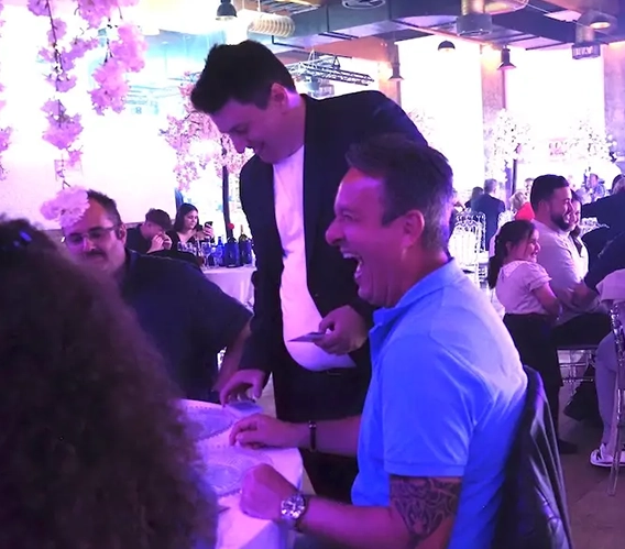 Mentalist Florian Dolar zeigt einem lachenden Gast am Tisch ein Kunststück während einer Hochzeitsfeier